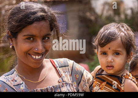 Nilavagilukaval, Karnataka, India - November 1, 2013: Closeup of smiling dark haired young mother with baby daughter on arm. Gold jewelry on both. Fad Stock Photo