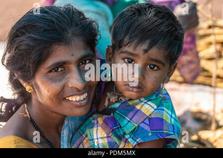 Nilavagilukaval, Karnataka, India - November 1, 2013: Closeup of smiling dark haired young mother with sad baby daughter on arm. Gold jewelry on both. Stock Photo