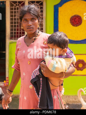 Nilavagilukaval, Karnataka, India - November 1, 2013: Closeup of staring dark haired young mother in pink dress with thickly clothed baby daughter on  Stock Photo
