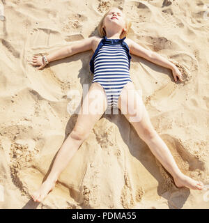 Girl making angel in sand on beach, high angle view