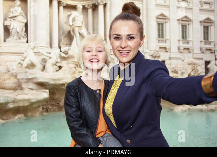 smiling modern mother and child tourists taking selfie against Trevi Fountain Stock Photo