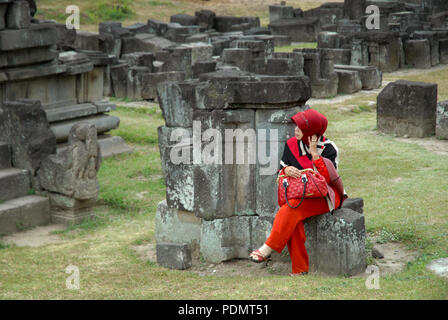 Lady in red sat on some stones, Prambanan temple, Yogyakarta, Java, Indonesia. Stock Photo