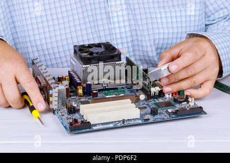 Man repairman is trying to fix using the tools on the computer that is on a workplace in the office. The concept of service electronics and computers. Stock Photo