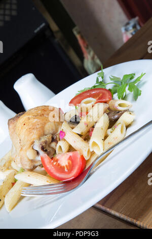 A plated meal of Pollo e Penne, Garlic infused roast Chicken thigh with Penne pasta and tomato, onion and mushroom