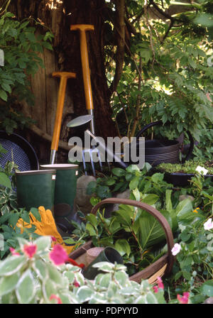 ASSORTED GARDEN TOOLS IN GARDEN SETTING (FORK, SPADE, BASKET, WATERING CAN, GARDENING GLOVES AND PLANT CLIPPINGS. Stock Photo