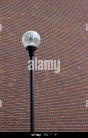 Single street light post with globe cover in front of a reddish brown brick wall background Stock Photo