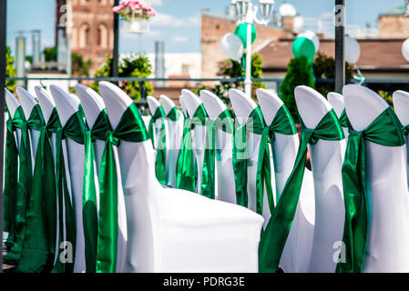 White wedding chairs with green ribbon outdoors Stock Photo