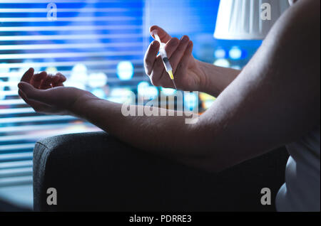 Heroin addict using drugs with injection needle and syringe in dark. Junkie injecting late at night. Dramatic addiction, overdose and substance abuse. Stock Photo