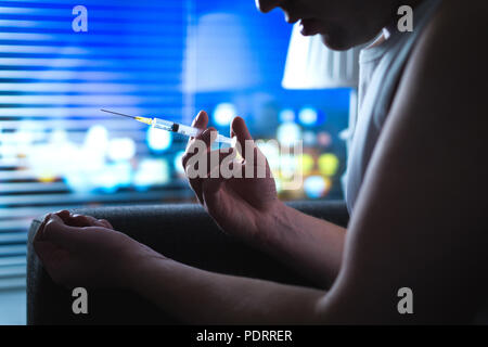 Heroin addict in dark late at night using drugs. Young man with bad drug problem using dirty needle. Dramatic addiction, overdose and substance abuse. Stock Photo