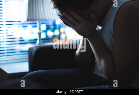 Sad and unhappy man covering face with hands in dark by window. Burnout, overwork or bankruptcy. Heartbroken person missing at night. Stock Photo
