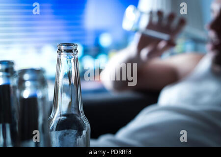 Anynomous alcoholic taking sip of beer. Home full of empty bottles. Alcoholism and drinking problem concept. Man sipping alcohol late at night. Stock Photo