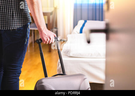 Man pulling suitcase and entering hotel room. Traveler going in to room or walking inside motel with luggage. Travel and holiday apartment rental. Stock Photo