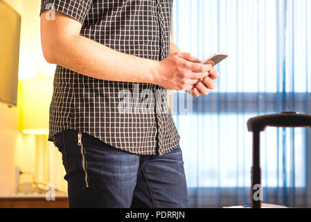 Smartphone in hotel room. Login to free hotel wifi and internet access. Traveler with mobile phone. Young man using cellphone. Stock Photo