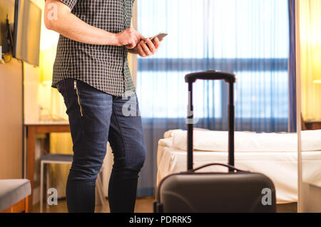 Man using smartphone in hotel room with baggage and suitcase. Tourist with mobile phone in holiday rental apartment. Calling taxi cab . Stock Photo