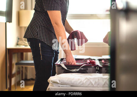 Man packing suitcase for vacation. Person putting clothes to baggagge in hotel room or home bedroom. Traveler with open luggage on bed. Stock Photo