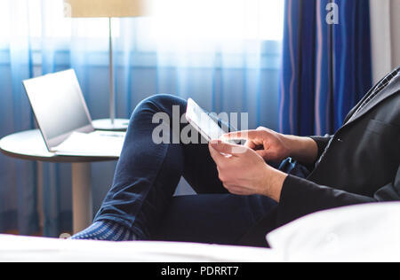 Business man reading news or email with tablet in hotel room. Businessman using smart mobile device and relaxing. Stock Photo