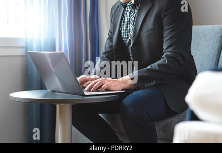 Business man working with laptop in hotel room. Businessman doing remote work with computer. Person sitting and typing. Stock Photo