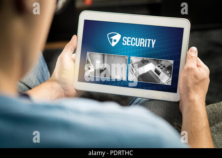 Man using home security system and application in tablet. Watching protection camera live footage inside a house or apartment. Stock Photo