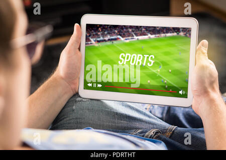 Man watching sports on tablet. Football and soccer game live stream and video player on screen. Pay per view (PPV) service. Stock Photo