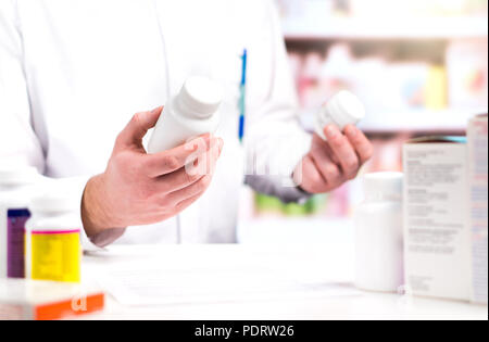 Pharmacist in pharmacy. Holding two bottles of pills and medicine. Professional druggist comparing medication. Man in white coat with tablets. Stock Photo