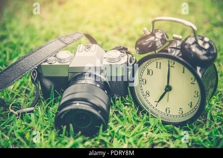 Photography times concept, mirrorless vintage camera with old bell clock on grass outdoor. Stock Photo