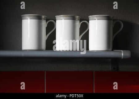 Three white coffee mugs lined up on a metal shelf. Stock Photo