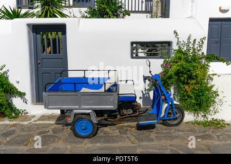 Motor tricycle with basket parked against whitewashed house.A three-wheeled blue motorcycle vehicle without people parked next to a white wall at Myko Stock Photo