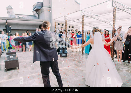 The back view of the dancing newlywed couple in the rain of confetti. Stock Photo