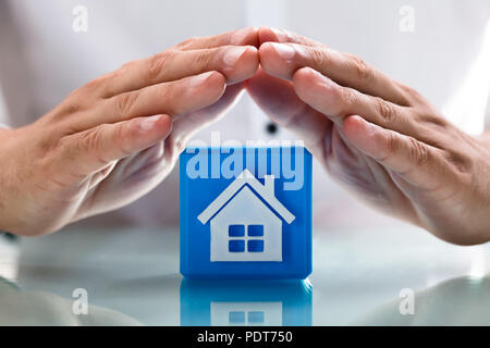 Close-up of a person's hand protecting blue cubic block with house icon Stock Photo