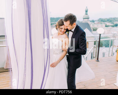 The sensitive portrait of the groom hugging the bride back on the balcony. Stock Photo