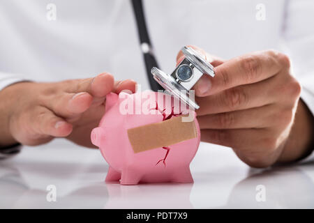 Doctor's hand examining broken pink piggybank with stethoscope Stock Photo