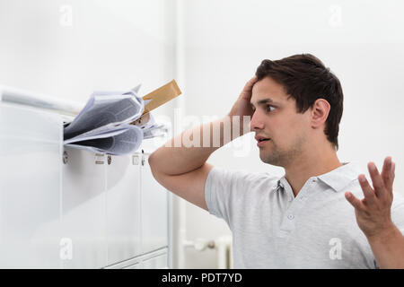 Close-up of man with hand on head in front of overloaded mailbox with junk mail Stock Photo