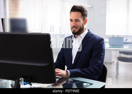 Smiling Young Businessman Using Computer In Office Stock Photo
