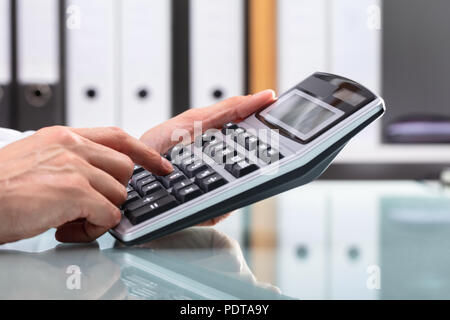 Businessperson's Hand Using Calculator Over Reflective Desk Stock Photo