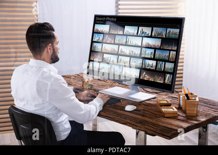 Young Male Photo Editor Searching Photos On Computer In Office Stock Photo