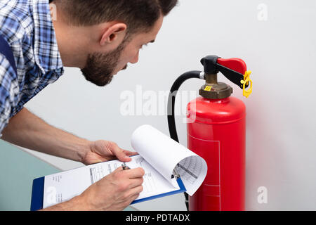 Close-up Of A Young Male Technician Checking Fire Extinguisher Writing On Document Stock Photo