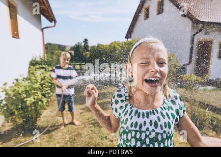 Children having fun with splashing water. Siblings on the back yard of the house during summer day. Stock Photo