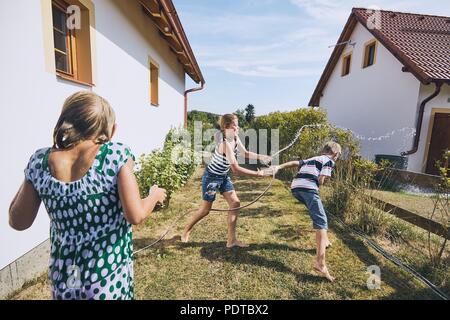 Children having fun with splashing water. Siblings on the back yard of the house during summer day. Stock Photo