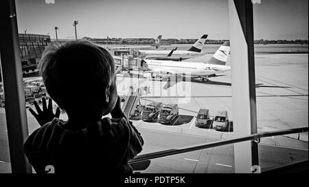 2-year old boy longingly watches the airplanes through the window of an airport terminal (editorial use) Stock Photo