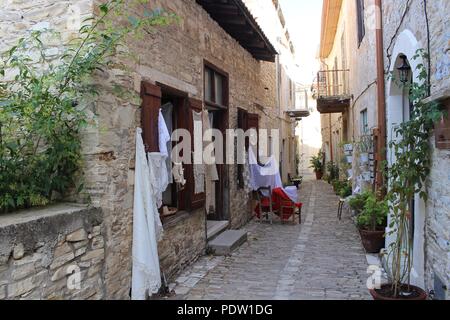 Narrow street in Larnaca. Narrow walking road between traditional stone houses in Cyprus with lace hanging outside. Stock Photo