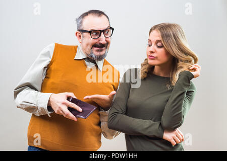 Nerdy man is trying to get attention from a beautiful woman by showing her his wallet full of money but she is still not interested. Stock Photo