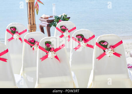 Back side of a group of white spandex wedding chairs cover with red pink organza sash for beach wedding venue settings Stock Photo