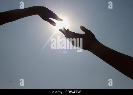 Two hands trying to connect in front of afternoon sun Stock Photo
