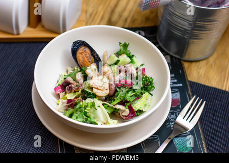 Warm salad with seafood mussels, octopus and fresh vegetables in deep plate on the table Stock Photo