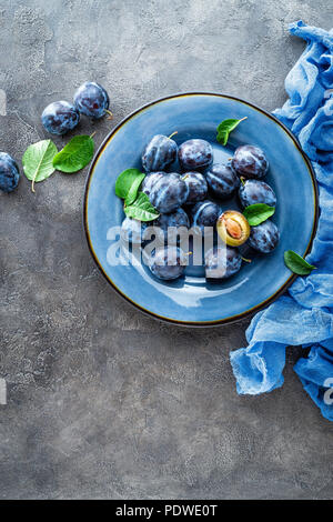 Fresh juicy sweet plums on plate with leaves Stock Photo