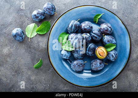 Fresh juicy sweet plums on plate with leaves Stock Photo