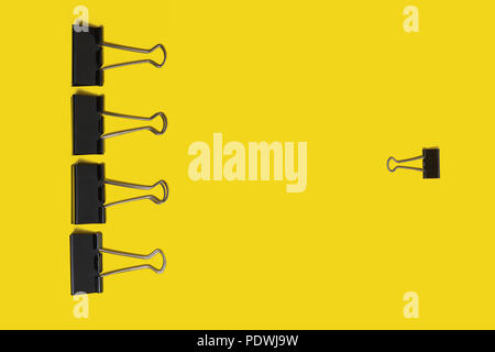 four big paper clips against small one lying on a yellow background Stock Photo