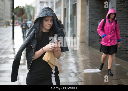 A woman uses her jacket to shelter from the heavy rain in Westminster, London. Stock Photo