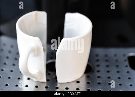 Close up on white espresso coffee cup broken in half placed on home espresso machine. Concept of bad morning Stock Photo