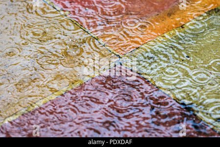 Woking, Surrey, England, UK, 10th August 2018. Heavy rain showers  fall in Woking, Surrey, south-east England after a period of prolonged drought. The shower and falling raindrops splash and make ripples in standing water on the colourful paving slabs of a garden patio. Credit: Graham Prentice/Alamy Live News. Stock Photo